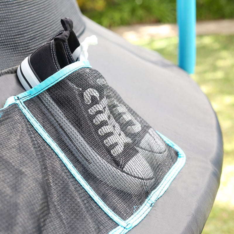 A pair of black sneakers stored in a mesh pocket attached to a TP Genius Blue 14ft Round Trampoline enclosure mat.