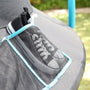 A pair of black sneakers stored in a mesh pocket attached to a TP Genius Blue 14ft Round Trampoline enclosure mat.