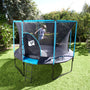 A child jumps on a TP Genius Blue 14ft Round Trampoline with a blue-framed SurroundSafe enclosure in a backyard.