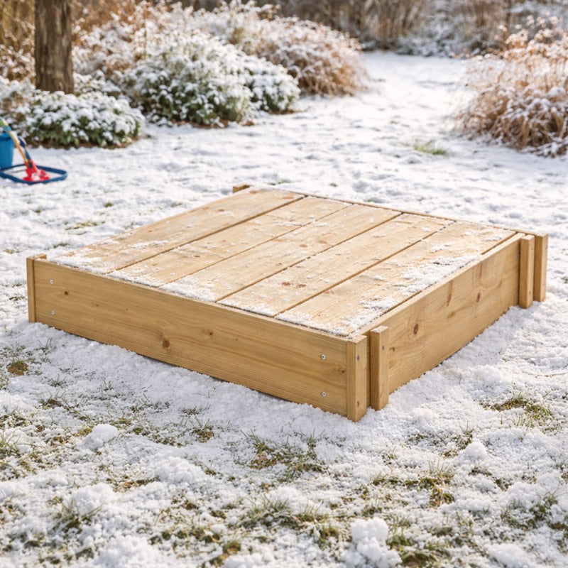 The TP Toys TP Wooden Lidded Sandpit - FSC® certified sits closed on a snow-dusted lawn, waiting for warmer days to invite outdoor play back to the garden.