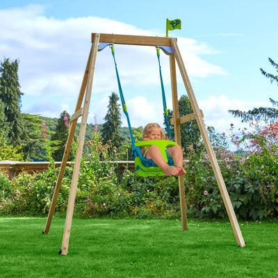 A young child enjoys the TP Toys TP Forest Wooden Single Swing with Quadpod—an FSC® certified set—hanging in a grassy garden among trees and flowers.