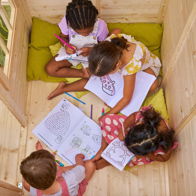 Four children color and draw with pencils and activity books while sitting on cushions inside the TP Toys TP Forest Cabin Wooden Playhouse, which is FSC® certified.
