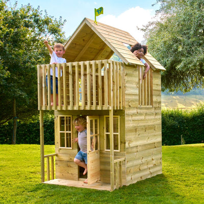 Four children enjoy the TP Toys TP Loft Two Storey Wooden Playhouse – FSC® certified; two are on the balcony (one waving) while others exit and look out, all playing in a grassy yard.