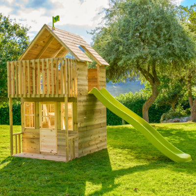 The TP Skye Two Storey Wooden Playhouse by TP Toys is made from FSC® certified timber and features a balcony plus a wavy green slide. This stylish playhouse stands on a grassy lawn, surrounded by trees and sunshine.