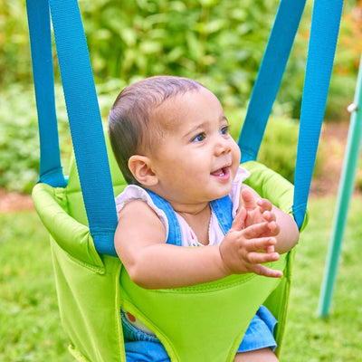 A baby enjoys the TP Foldaway Baby Swing by TP Toys, smiling and clapping hands with lush greenery in the background.