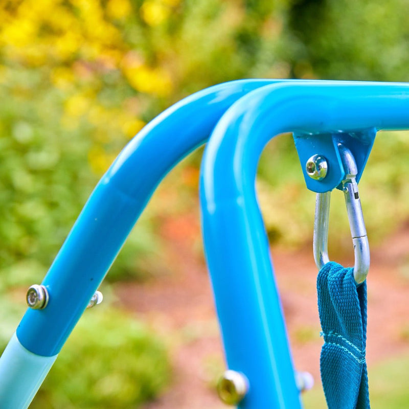 Close-up of a blue TP Toys TP Foldaway Baby Swing frame with a carabiner on a fabric strap, set against a blurred outdoor background—ideal for those seeking a sturdy indoor-outdoor baby swing.