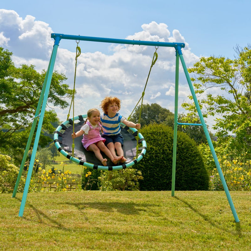 Two children sit together on the TP Toys Giant Nest, part of the TP Giant Nest Metal Swing Set, enjoying a sunny day in a grassy garden.