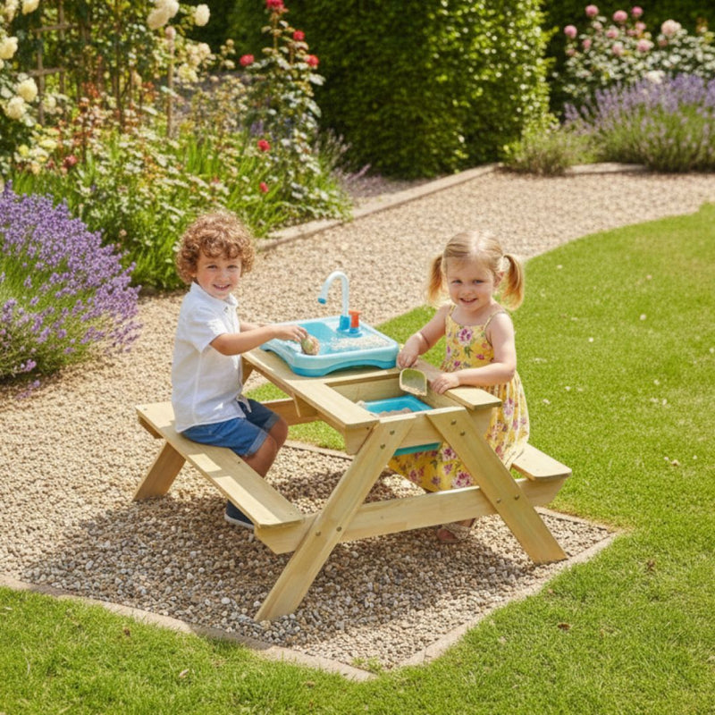 Two young children play happily with water at the TP Toys TP Splash & Play Wooden Picnic Table in a sunny garden filled with flowers and greenery.