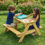 Two children sit at the TP Toys TP Splash & Play Wooden Picnic Table outdoors; one uses the working sink feature, while the other colors with markers on paper.