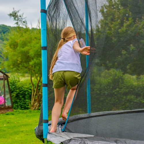 A child with long hair climbs through the net entrance of a TP Toys TP Up 14ft Trampoline in a grassy backyard.