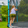 A child with long hair climbs through the net entrance of a TP Toys TP Up 14ft Trampoline in a grassy backyard.