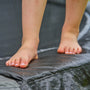 Close-up of a person’s bare feet on the edge of the TP Toys TP Up 14ft Trampoline—ideal for kids to enjoy outdoor fun.