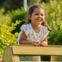 A young girl in a floral dress smiles behind the TP Toys TP Wooden Toddler Climb & Slide—FSC® certified—ready for active play in a sunlit garden.