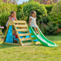 Three young children enjoy active play on the TP Toys TP Wooden Toddler Climb & Slide – FSC® certified, set up in a grassy garden surrounded by flowering plants.