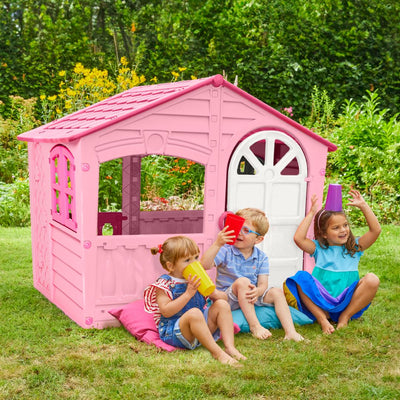 Three young children play with colorful cups on the grass beside the TP Toys Palplay Plastic Playhouse of Fun - Candy Floss Edition in a vibrant garden.