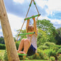 A child climbs the rope ladder of the TP Knightswood Double Wooden Swing Set With Glide Ride & Rope Ladder by TP Toys, which is crafted from PEFC certified wood and set outdoors among greenery under a blue sky.