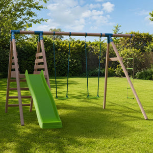 The TP Knightswood Double Wooden Swing & Slide Set With Rope Ladder by TP Toys, featuring a green 8ft slide, double swings, and a climbing rope ladder, is set up on a well-kept grassy lawn surrounded by trees and bushes under a blue sky.