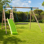 The TP Knightswood Double Wooden Swing & Slide Set With Giant Nest Swing & Rope Ladder by TP Toys features a green slide, circular swing, climbing rope ladder, and a giant nest swing, all set on a grassy yard with trees and bushes in the background.