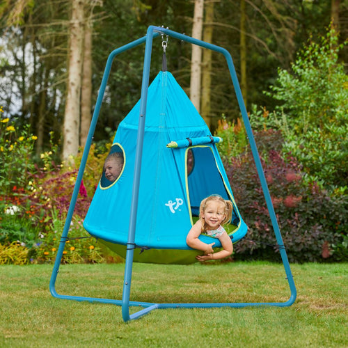Three children play inside the TP UFO Den & Metal Frame by TP Toys, a blue tent shaped like a UFO, hanging securely from its sturdy metal frame outdoors on a grassy lawn with trees and flowers in the background.