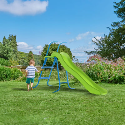 A young child enjoys the garden on a grassy lawn near the TP Toys TP 6ft (1.8m) Wavy Slide & Stepset with blue steps, surrounded by trees and bushes under a partly cloudy sky.