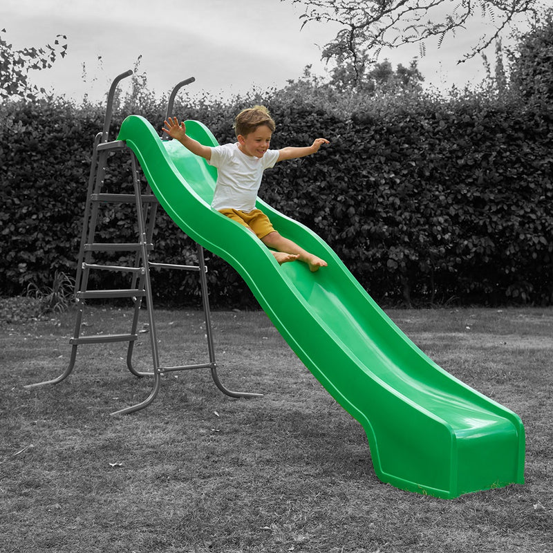 A young boy in a white shirt and yellow shorts slides down the bright green TP Toys 3m/10ft Super Wavy Slide in a grassy yard.
