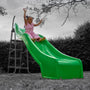 A young child in a pink outfit slides down the bright green TP 3m/10ft Super Wavy Slide by TP Toys, enjoying the UV stabilised outdoor play equipment in a yard surrounded by trees and bushes.