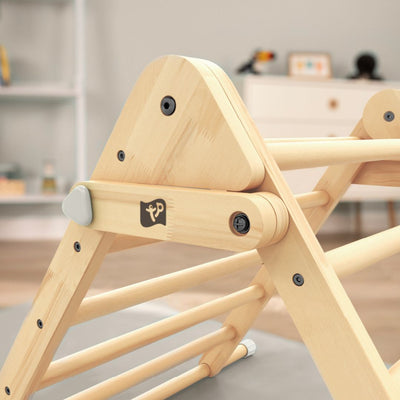 Close-up of the TP Toys TP Active-Tots Pikler Style Wooden Climbing Triangle - FSC® certified, featuring a logo, set in a room with blurred shelves and furniture in the background.
