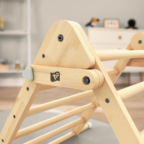 Close-up of the TP Toys TP Active-Tots Pikler Style Wooden Climbing Triangle - FSC® certified, featuring a logo, set in a room with blurred shelves and furniture in the background.