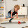 A young child climbs over the TP Toys TP Active-Tots Pikler Style Wooden Balance Board (FSC® certified) while reaching for a red toy train, building gross motor skills through active play in a fun, Montessori-inspired way.