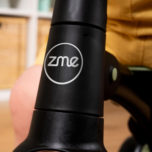 Close-up of a black object featuring the TP Toys logo, with part of a person in yellow—possibly riding the Zoomee Balance Bike to Trike—visible in the background.