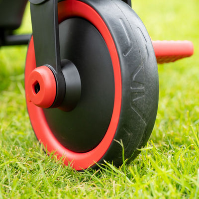 Close-up of a black and red plastic wheel on green grass, part of the TP Toys Zoomee 2 in 1 Trike – Firecracker, an adjustable handle tricycle for kids.