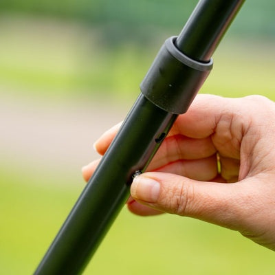 A hand adjusts the height of the Zoomee 2 in 1 Trike – Firecracker by TP Toys outdoors, pressing a spring-loaded locking button on its black metal pole.