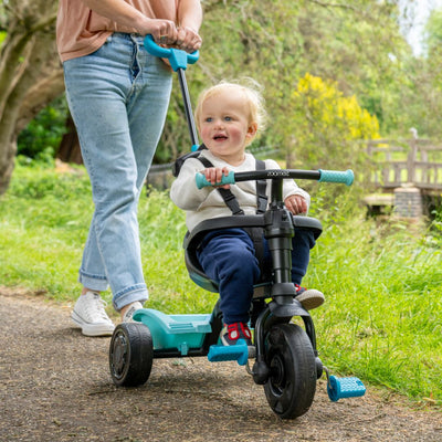 A child rides the TP Toys Zoomee 4 in 1 Trike - Dino Discovery, featuring a fun dinosaur print and adjustable UV sunshade.