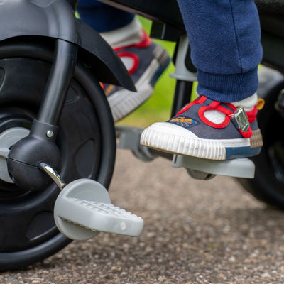 Close-up of a childs feet on the pedals of the TP Toys Zoomee 4 in 1 Deluxe Trike - Grey Storm, with the child wearing blue pants and sneakers.