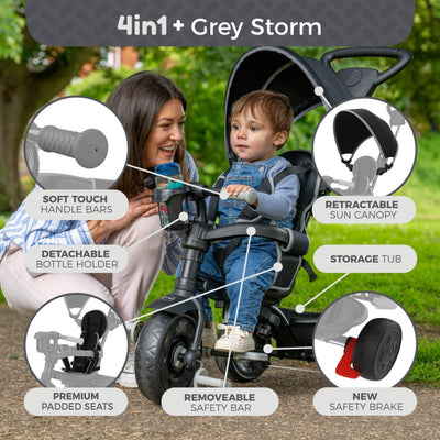 A woman kneels beside a child seated in the TP Toys Zoomee 4 in 1 Deluxe Trike - Grey Storm, which features an adjustable seat, handlebars, bottle holder, sun canopy, storage tub, padded seat, safety bar, and brake.