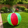 The TP Toys Hydro Watermelon Sprinkler is a fun inflatable water toy that sprays streams of water, perfect for backyard play on a green lawn. A garden and wooden fence complete the playful summer scene.