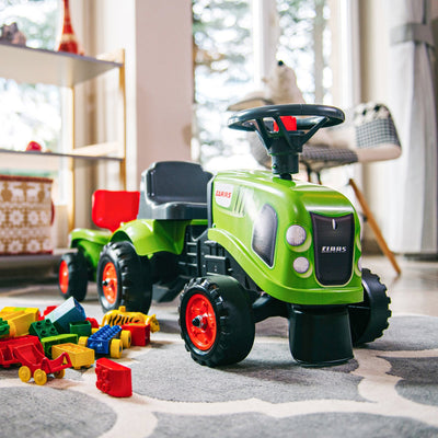 The TP Toys Falk Claas Baby Tractor, featuring a green body and red wheels, is displayed indoors on a patterned rug with colorful plastic building blocks scattered around.
