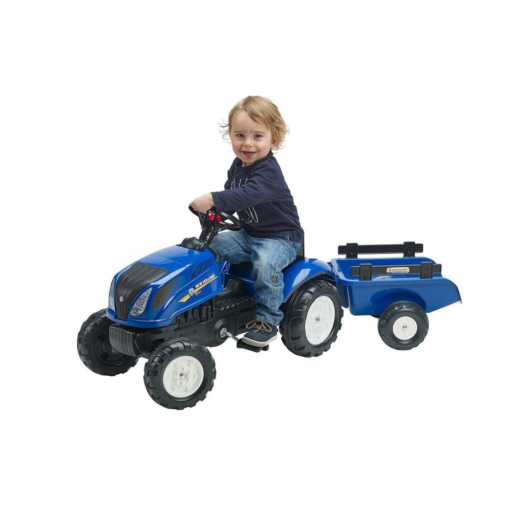 A young child smiles while sitting on a Falk New Holland Tractor with Trailer and Opening Bonnet by TP Toys, holding the steering wheel.