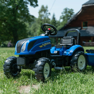 A blue Falk New Holland Tractor with Trailer and Opening Bonnet by TP Toys, featuring a black seat, is parked on green grass with a wooden house and trees in the background—this detailed replica looks ready for adventure.