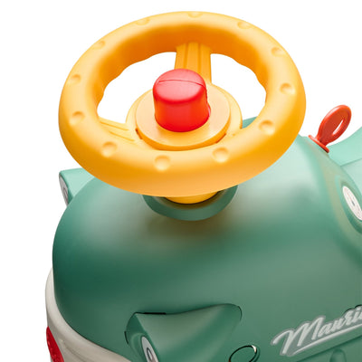 Close-up of the Falk Maurice Vintage Baby Green Tractor by TP Toys, featuring a yellow plastic steering wheel with a red center button and a walking aid bar for toddlers learning to walk.