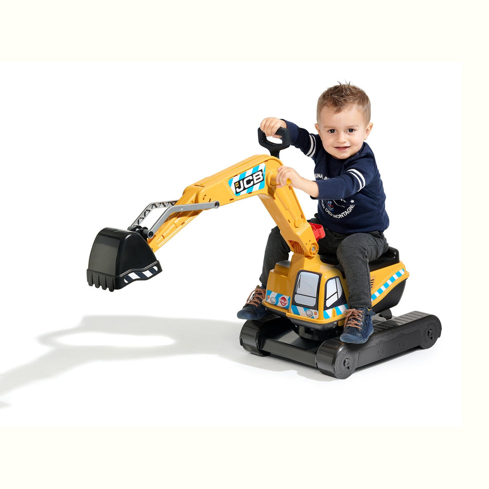 A young boy smiles as he sits on the TP Toys Falk JCB Fully Articulated Digger, wearing a helmet and holding the handle, with the mechanical arm of this ride-on excavator extended forward.