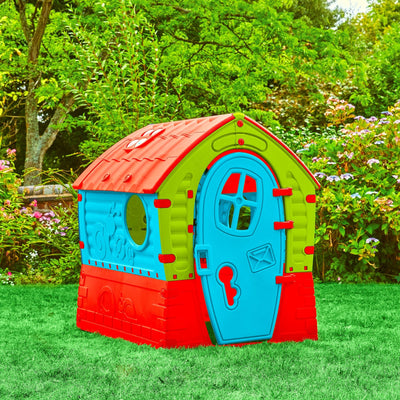 The TP Toys Palplay Plastic Dream Playhouse features UV resistance, a blue door, and a red roof. It stands on green grass in a garden surrounded by trees and flowers.