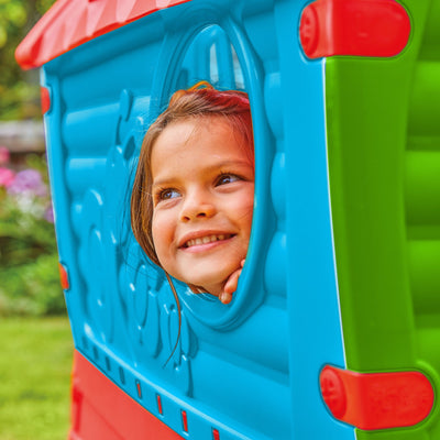A young child smiles and looks out the window of a colorful, UV-resistant TP Toys Palplay Plastic Dream Playhouse set up outdoors.