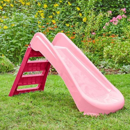 The TP Toys PalPlay Pink & White Plastic Folding First Slide stands on green grass in a garden, featuring red steps and surrounded by flowering plants in the background.