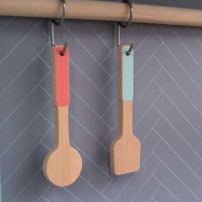 The Owl & Fox Wooden Imagination Kitchen Set by TP Toys features two wooden utensils with colorful handles, hanging from metal rings on a wooden rod—ideal for pretend play and inspiring creativity in any play kitchen.