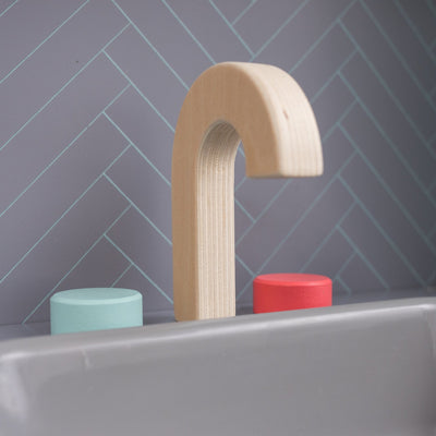 The TP Toys Owl & Fox Wooden Imagination Kitchen Set (FSC® certified) features a gray play sink with blue and red faucet knobs, set against a herringbone-patterned tile wall.