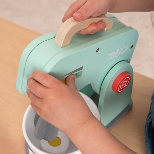 A child uses the TP Toys Owl & Fox Wooden Baking Set - FSC® certified, operating a light blue wooden mixer and holding a bowl—perfect for pretend play and inspiring creativity in any play kitchen.