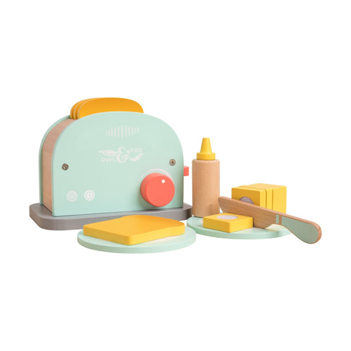 The TP Toys Owl & Fox Wooden Toaster Set—FSC® certified—features pastel colors, two bread slices, butter, a knife, and a bottle. Ideal Montessori playset for pretend play, shown on a white background.