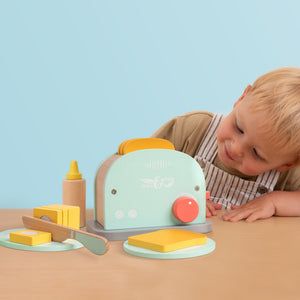 A young child admires the TP Toys Owl & Fox Wooden Toaster Set—an FSC® certified pastel playset with toy bread, butter, knife, and bottle—perfect for pretend play and Montessori activities.