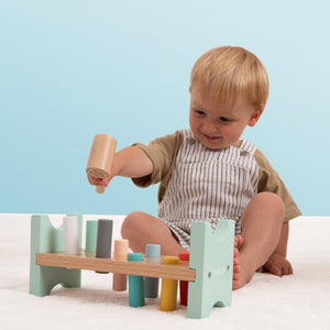 A young child sits on the floor using the TP Toys Owl & Fox Wooden Hammer Bench—FSC® certified—to build hand-eye coordination, playing with its pastel colors against a light blue background.